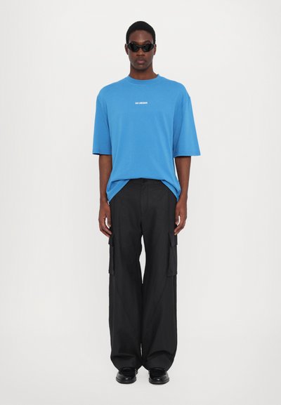 Blå oversized T-shirt med korta ärmar och vitt logotyp, tillsammans med svarta vida cargobyxor med sidofickor och rak nederkant.