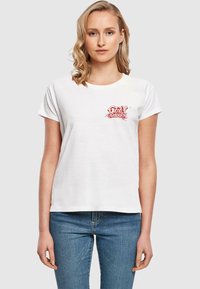 T-shirt en coton blanc avec un logo graphique rouge sur le côté gauche de la poitrine. Le t-shirt a des manches courtes et un col rond.
