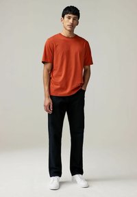 Kortærmet orange t-shirt parret med sorte bukser og hvide sneakers. T-shirten har en afslappet pasform og blød tekstur.
