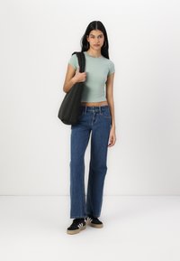 Top crop ajustado verde claro, jeans de perna larga azuis, mala a tiracolo preta e ténis pretos com riscas brancas. Design simples, estilo casual.