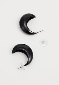 Sorte halvmåneformede øreringer lavet af skinnende materiale, med en stud post og inkluderede klare gummibagsider for sikker bæring.