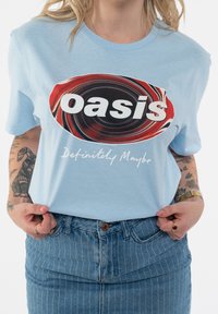 Light blue cotton t-shirt featuring a circular graphic with red and black swirls and bold white text "oasis" above "Definitely Maybe."