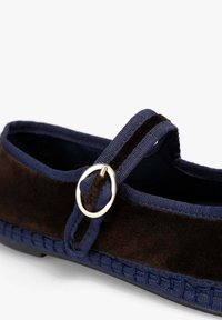 Zapato de ante marrón oscuro con una correa de tela azul marino, que presenta una hebilla circular de plata y costuras texturizadas a lo largo de la suela.