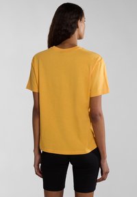 Korte mouwen gele t-shirt van katoen met een ronde halslijn, relaxte pasvorm en zijsplitten aan de onderkant, gecombineerd met zwarte shorts.