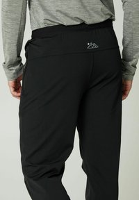 Schwarze Sporthose mit glatter Textur, elastischem Bund und seitlichen Reißverschlusstaschen, mit einem kleinen Berg-Logo auf der Rückseite.