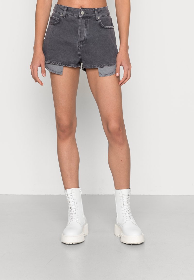 Pantalones cortos de mezclilla gris de cintura alta con dobladillos enrollados y bolsillos frontales, combinados con botas de tobillo blancas con cordones. Textura suave, diseño informal.