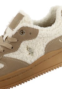 Baskets beige et blanches avec tissu sherpa, semelle marron, lacets beige et petit logo argenté de deux joueurs de polo sur le côté.