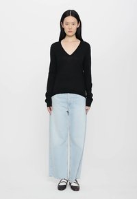 Zwarte langoudsweater met V-hals, gecombineerd met lichtblauwe wijdvallende jeans, wat een casual ensemble creëert. Slank, zachte textuur met een relaxte pasvorm.