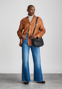 Woman in brown leather jacket, striped turtleneck, blue wide-leg jeans, black handbag over shoulder, and black shoes.