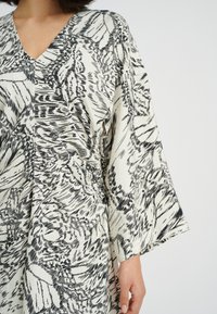 Tunika i svartvitt mönster har en V-ringning, breda ärmar och mjukt tyg med en flödande design, accentuerad av texturvariationer.