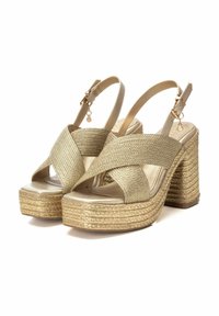 Sandalias doradas tipo slingback con textura tejida, diseño de tiras cruzadas y una plataforma y tacón gruesos estilo cuerda, que cuentan con correas en el tobillo ajustables.