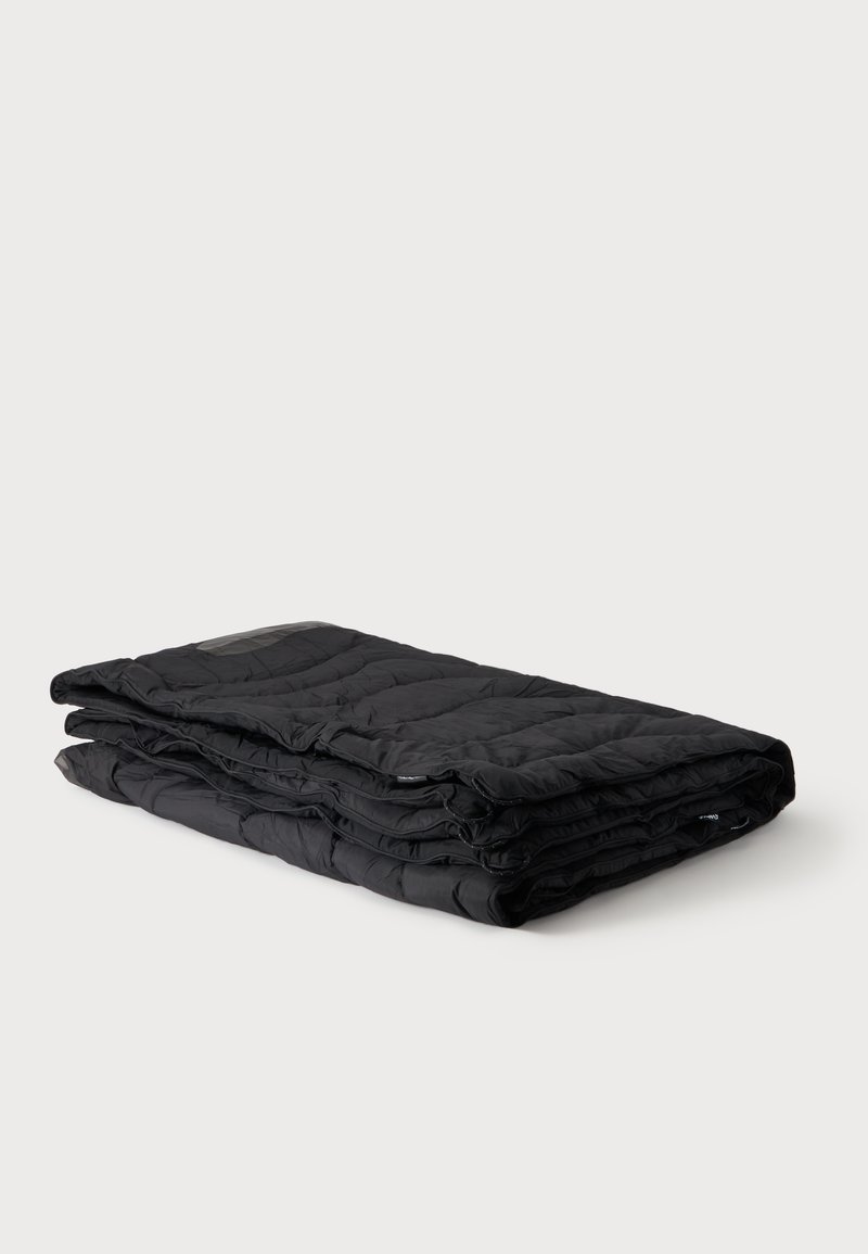 Couverture matelassée noire pliée soigneusement, présentée sur un fond gris clair uni.