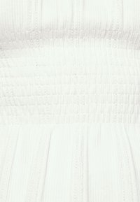 Weiße Stoff mit einer strukturierten, gerippten Musterung, die oben raffinierten Details und unten fließenden Falten aufweist.