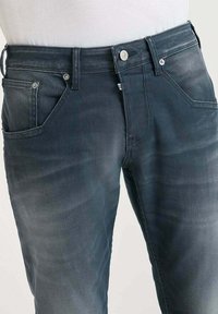 Jeans de mezclilla azul oscuro con una textura ligeramente deslavada, que cuentan con un diseño clásico de cinco bolsillos y detalles metálicos en la cintura.