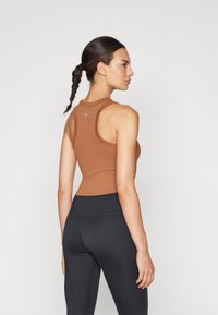 Smeđi uski top s racerback dizajnom, s malim plavim logom. Uparen s crnim tajicama visokog struka, glatke teksture.