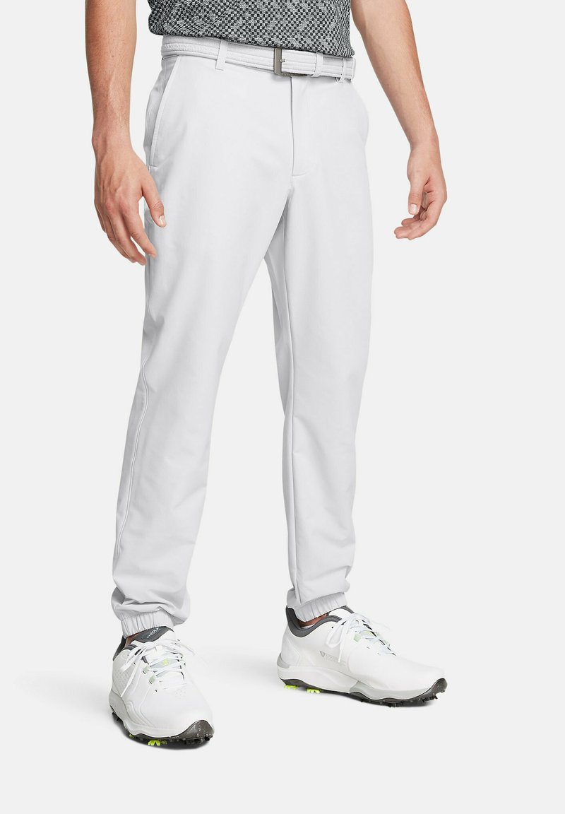 Pantalones de golf blancos con piernas entalladas, puños elásticos y una camisa polo negra texturada; combinados con zapatos de golf blancos con detalles verdes.