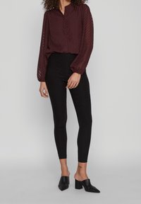 Blouse bordeaux à manches longues avec un motif en chevrons et un bouton devant, associée à des leggings noirs taille haute et des mules à talons carrés.