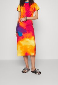 Šaty s tzv. tie-dye vzorem v živých barvách žluté, oranžové, růžové a modré. Krátké rukávy, střední délka s volným střihem. Nosit s zdobenými sandály.