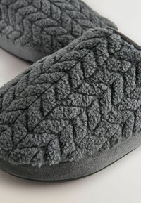 Šedé pantofle vyrobené z texturovaného, huňatého materiálu s tkaným vzorem. Měkký svršek s odolnou podrážkou pro pohodlí.