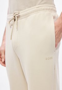 Beżowe spodnie dresowe wykonane z miękkiego materiału, z elastycznym pasem, sznurkiem do regulacji oraz subtelnym logo "BOSS" na kieszeni.