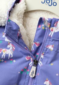 Lila Kinderjacke mit Einhornmuster, Fleece-Futter und einem Frontreißverschluss mit einem Marken-Zieher. Blumen und farbenfrohe Akzente.