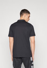 Svart polo skjorte med korte ermer, laget av glatt stoff, med klassisk krage og slim fit. Synlig logo på ermet.