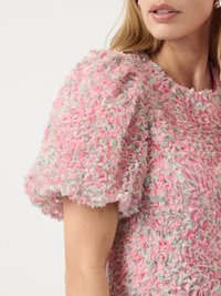 Teksturert rosa topp med puffete ermer, laget av et mykt, fluffy stoff med hints av mintgrønn og hvite detaljer. Rund hals.