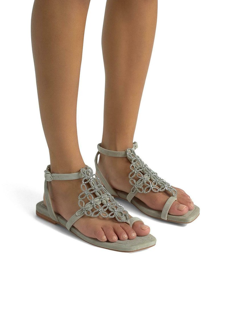 Sandales thong de couleur gris clair avec une embellissement en perles, semelle plate et bride de cheville. Matériau en daim doux et design ouvert à l'avant.