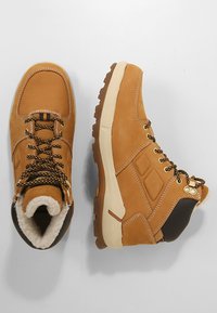 Bottes de randonnée en daim marron avec une semelle en caoutchouc épaisse, des lacets et une doublure en fausse fourrure. Présente des accents beige et un renfort au niveau du talon.