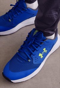 Blaue Sportschuhe aus Mesh und synthetischen Materialien. Mit kontrastierenden gelben Akzenten, einer strukturierten Oberfläche und einer Gummisohle.