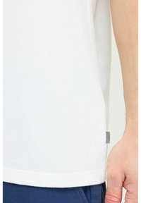 Hvid bomulds T-shirt med korte ærmer, lige kant og et lille sort-hvidt mærke i sidesømmen. Blød, glat tekstur.
