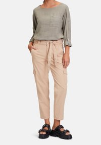 Olivgrön linneblus med långa ärmar och bröstfickor, kombinerad med beige cargobyxor med bälte och sidofickor. Svarta sandaler.