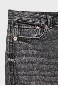 Mustat farkut, joissa on hienovarainen testi, pronssinvärisillä varusteilla, etutaskuilla ja tavanomaisella vyötäröllä.