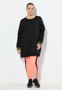 Abito felpato nero con dettagli gialli, indossato su leggings rosa con strisce laterali nere, abbinato a scarpe da ginnastica nere.