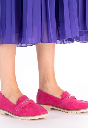 Mocassins en daim rose à bout arrondi, avec une bandoulière décorative et un subtil accent métallique, associés à une jupe plissée violet fluide.