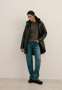 Czarna pikowana kurtka z kapturem noszona na szarym swetrze, w połączeniu z jasnoniebieskimi spodniami typu wide-leg i masywnymi czarnymi botkami. Gładka tekstura i luźny krój.