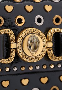 Borsa a tracolla in pelle nera adornata con borchie d'oro e d'argento, particolari a forma di cuore e una fibbia decorativa con un design emblematico centrale.