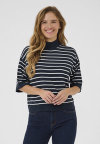 Navy and white striped knit top with a high neckline and short sleeves, paired with dark jeans. Soft texture, relaxed fit.