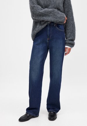 Blue high-waisted wide-leg jeans made of denim, featuring orange stitching and a traditional five-pocket design, paired with a grey fluffy sweater.