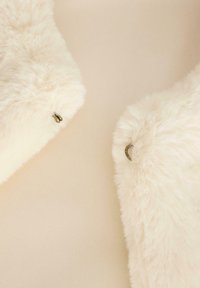 Faux fur kraag in crèmekleur met een zachte textuur en twee donkere metalen sluitingen om te bevestigen. Achtergrond in lichtbeige.