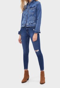 Blue denim jacket with two front pockets and distressed blue skinny jeans. Brown ankle boots with a low heel complete the outfit.