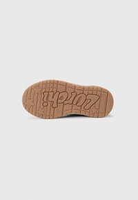 Gumová podrážka topánky v svetlohnedej farbe s hviezdičkovými vzormi a výrazne zobrazeným logom "Vans". Hladký povrch s textúrovanými zónami gripu.