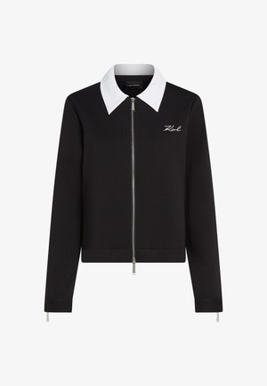 Juodas užtraukiamas džemperis su kontrastinga balta apykakle, turintis liesą siluetą ir išsiuvinėtą logotipą kairėje krūtinės pusėje. Lygi tekstūra.