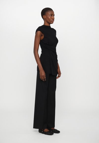 Top negro sin mangas con diseño drapeado, combinado con pantalones de pierna ancha de talle alto en negro. El conjunto presenta una textura suave y líneas limpias.