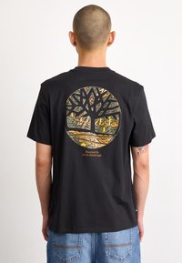 Camiseta de algodón negra con un gráfico circular en la parte posterior que presenta un diseño de árbol en tonos tierra. Manga corta y corte relajado.