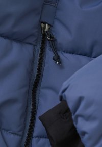 Marinblå puffjacka i tyg med dragkedja, med en svart dragkedja och en justerbar snodd. Mjuk textur och vadderad design.