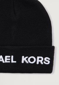 Zwarte gebreide beanie met ribbelstructuur en een omgeslagen rand, voorzien van witte geborduurde tekst "MICHAEL KORS" op de voorkant.