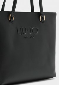 Czarna torba typu tote wykonana z teksturowanej sztucznej skóry, z wytłoczonym logo "LIU·JO MILANO" oraz złotymi elementami ozdobnymi.