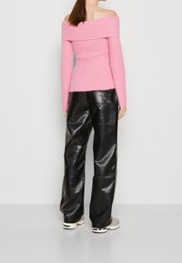 Różowy sweter z dekoltem off-the-shoulder, dziany, o dopasowanej sylwetce. W połączeniu z czarnymi, luźnymi skórzanymi spodniami i szarymi trampkami.