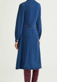 Robe en jean bleu foncé avec ceinture tissée. Manches longues avec poignets boutonnés. Coupe droite, longueur mi-mollet, tissu texturé.